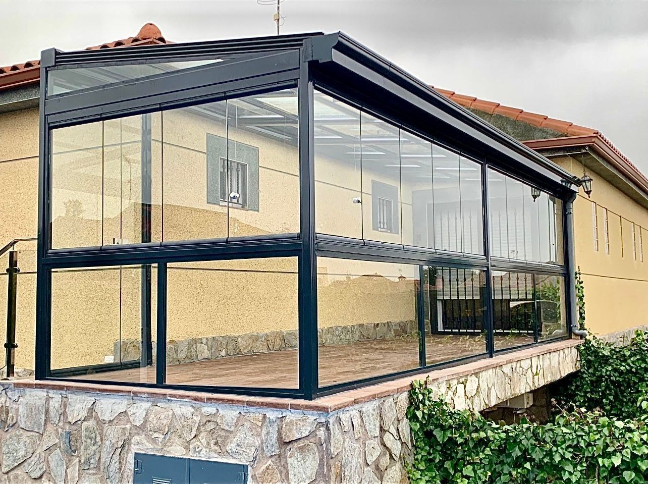 Anexo acristalado con estructura negra, unido a un edificio de color claro con base de piedra.