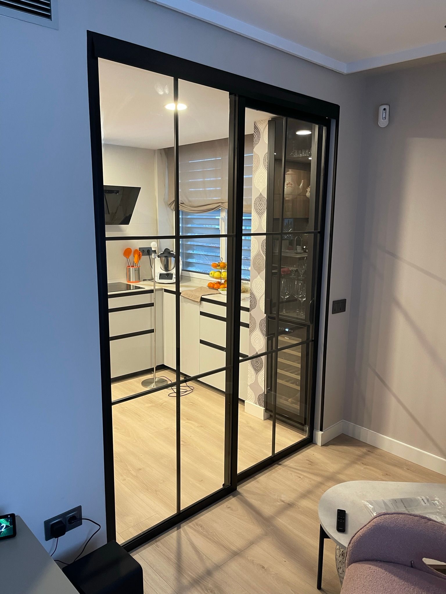 Salón moderno con sofá marrón y puerta de cristal de suelo a techo, cuadro enmarcado en blanco.