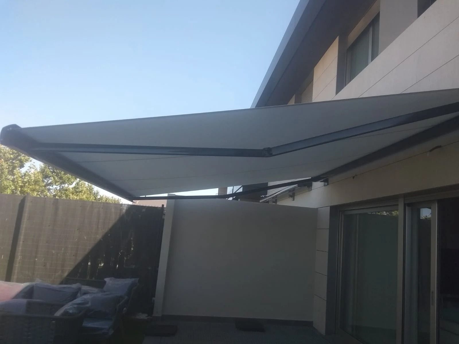 Un toldo blanco cubre un área de patio frente a una casa.