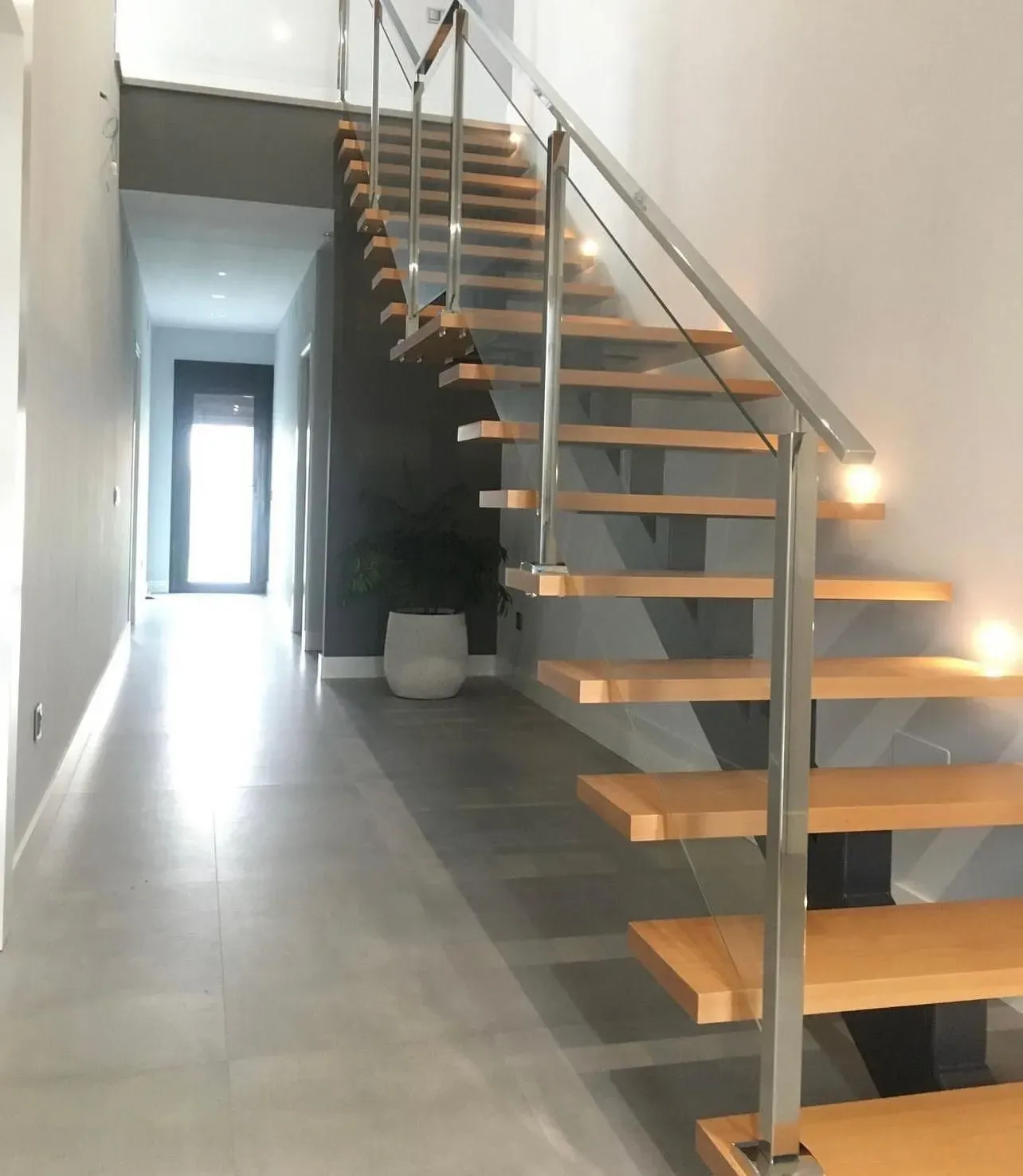Una escalera con escalones negros y barandilla de cristal.