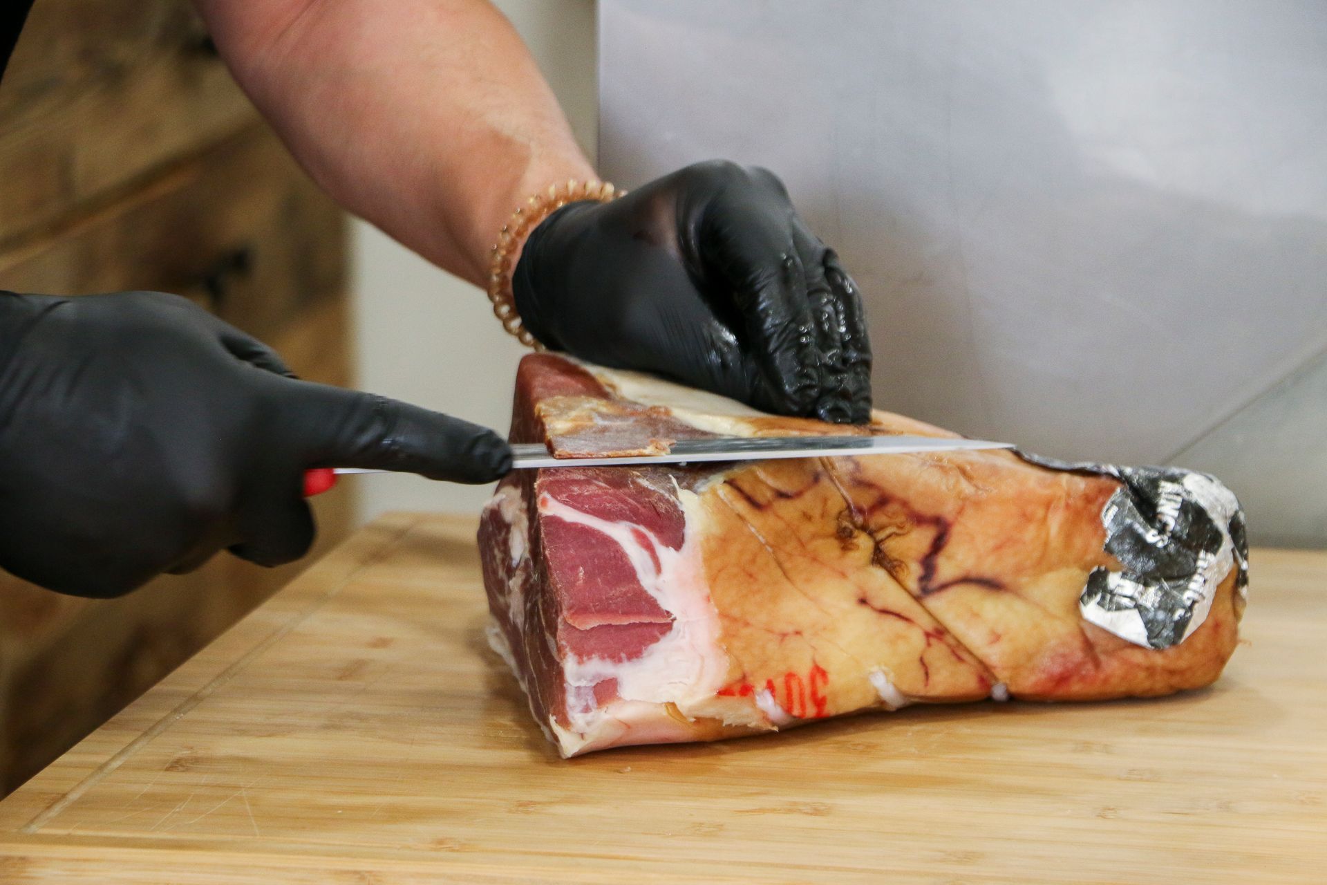 Main gantée qui découpe un jambon