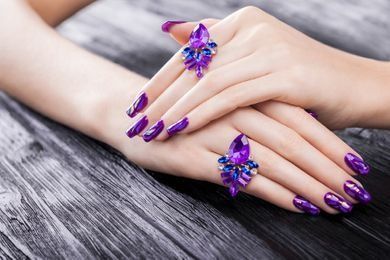 Manos de mujer con uñas moradas y un anillo en el dedo.