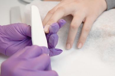 Una mujer se hace las uñas con un técnico de uñas que usa guantes morados.