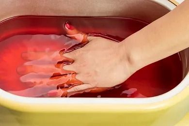 La mano de una mujer está en un recipiente con líquido rojo.