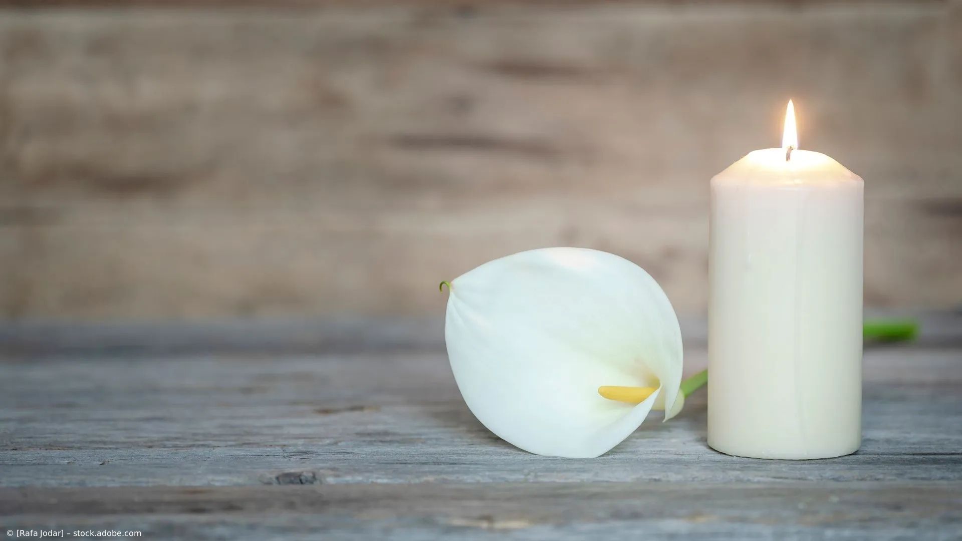Weiße Blume und brennende Kerze auf einer rustikalen Holzoberfläche.