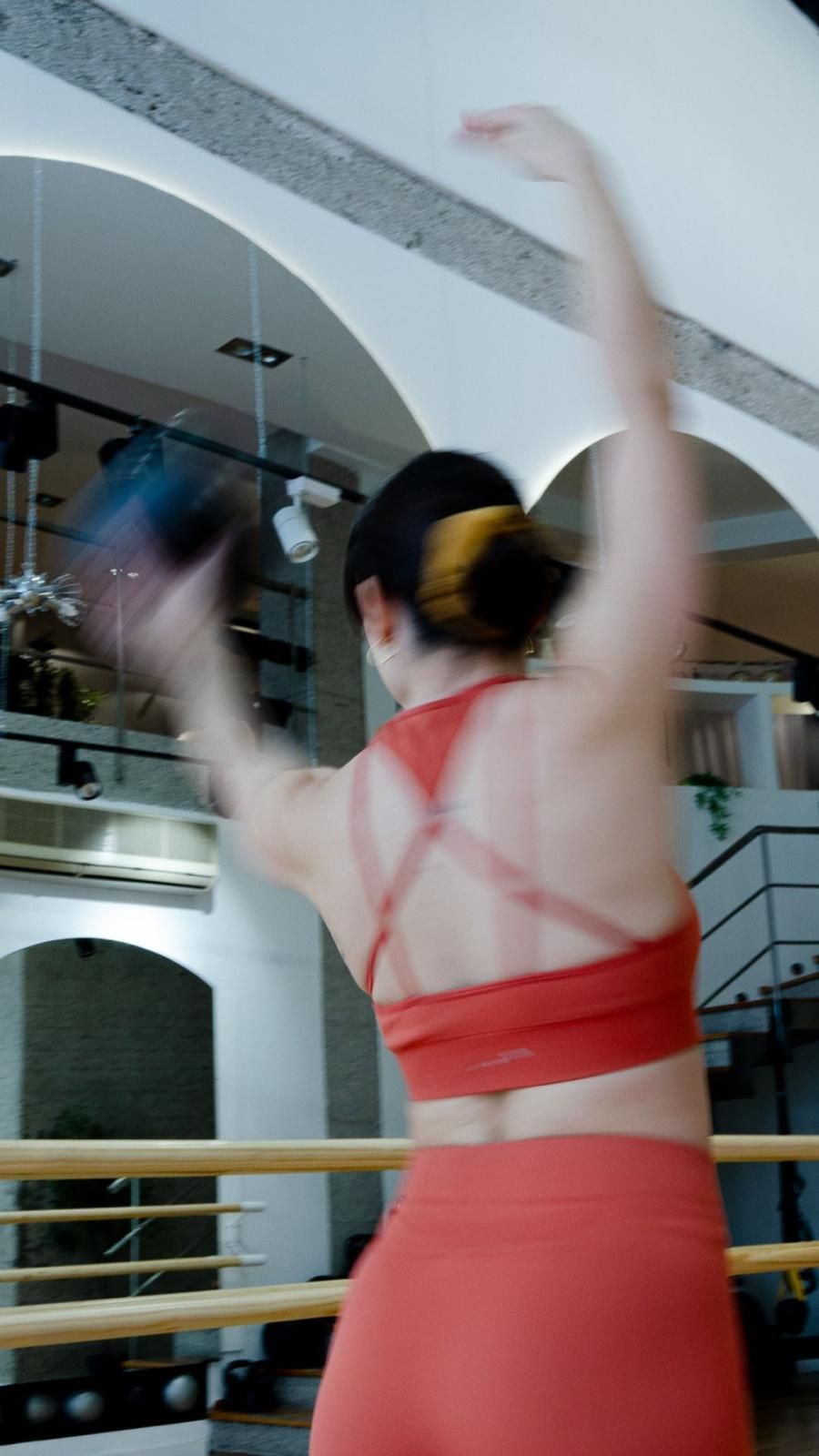 Una mujer con un sujetador deportivo rojo y pantalones cortos rojos está parada frente a un espejo en un gimnasio.