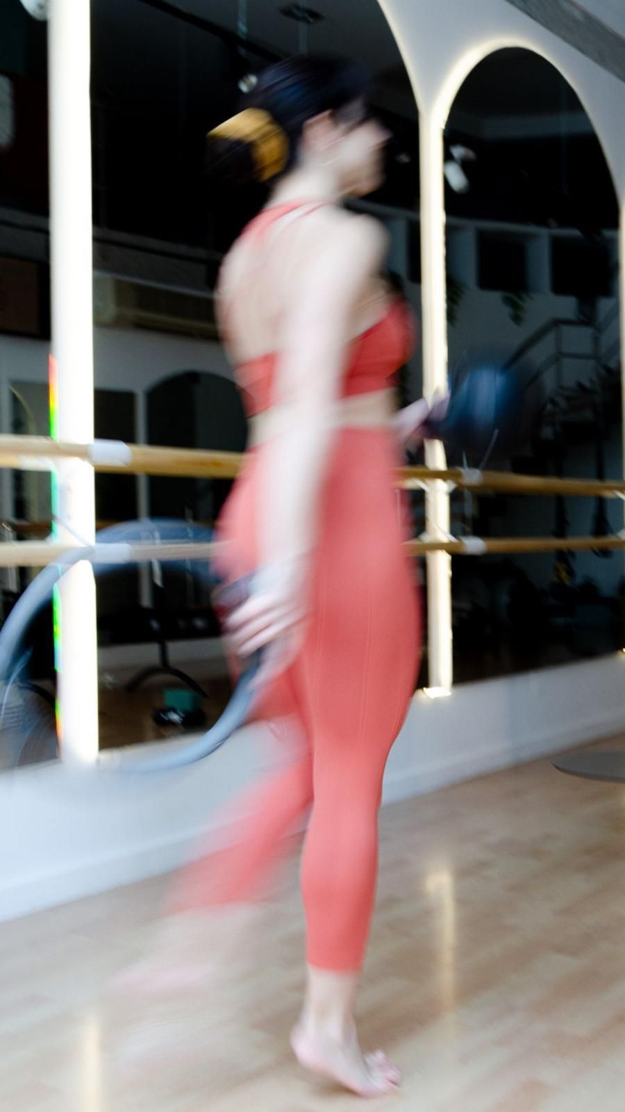 Una mujer con pantalones rojos sostiene un hula hula en un gimnasio.