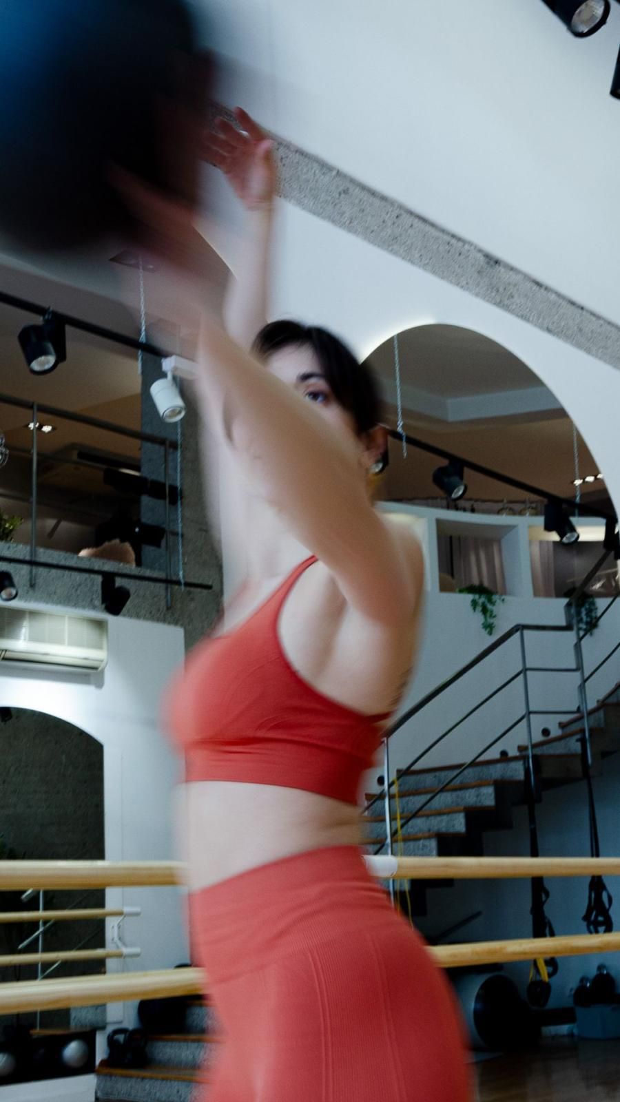 Una mujer con una camiseta roja y pantalones cortos está lanzando una pelota en un gimnasio.