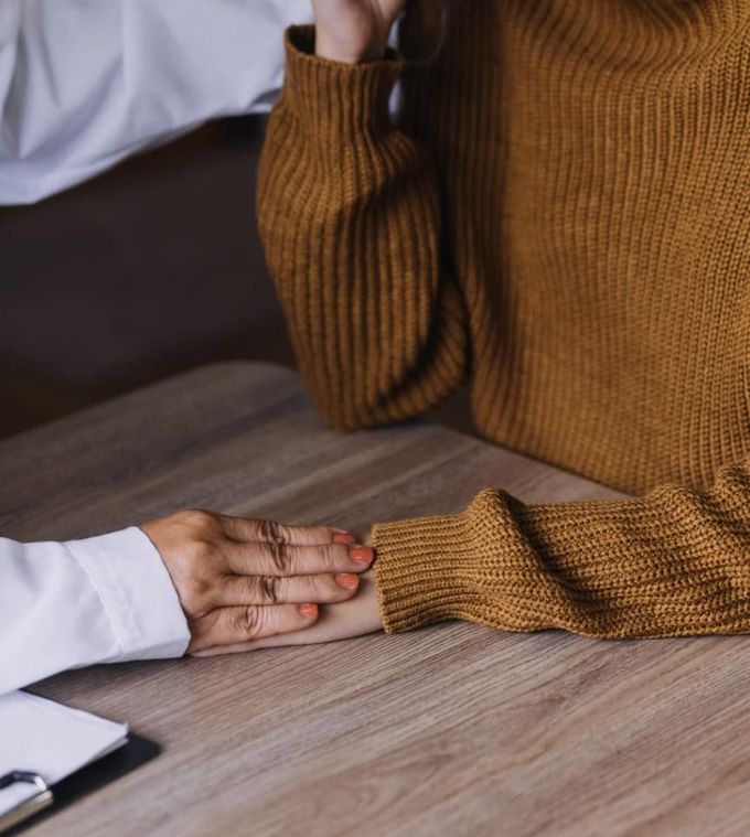 Una persona con bata blanca de médico apoya su mano reconfortantemente sobre la mano de una persona