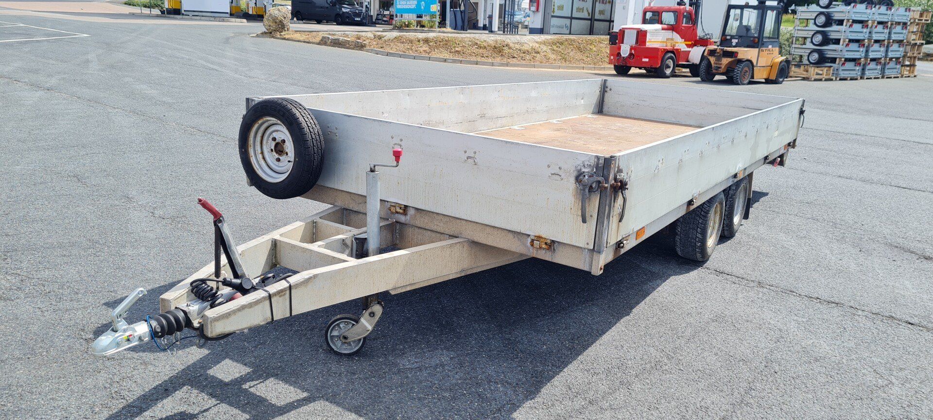 Pritschenanhänger auf einem asphaltierten Parkplatz mit angebrachtem Ersatzreifen.