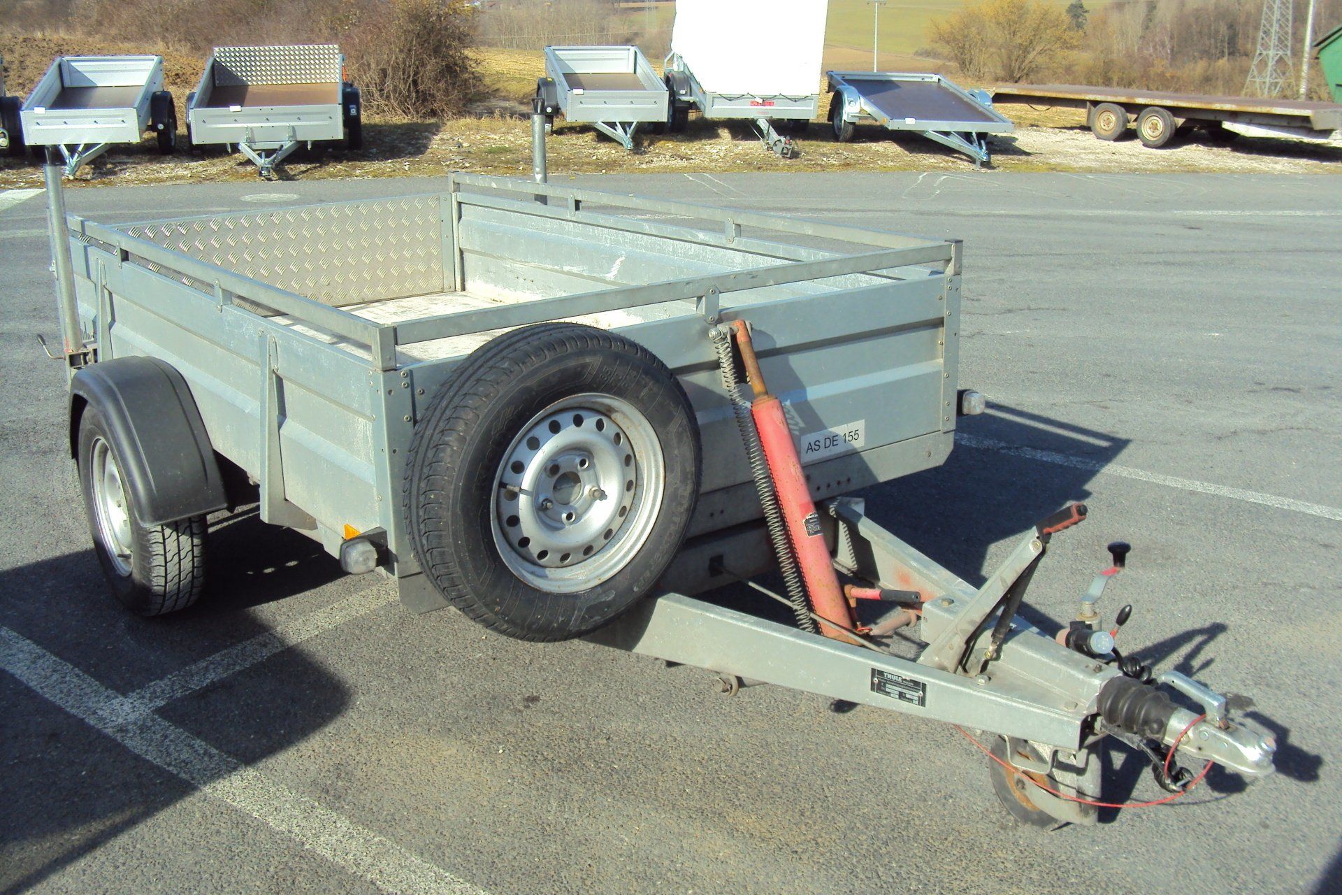 Silberner Nutzanhänger mit Ersatzreifen auf einem Parkplatz.