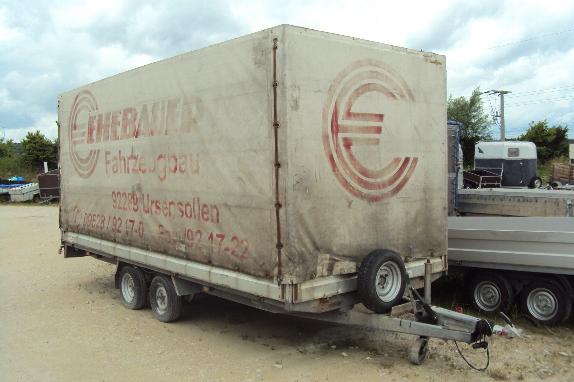 Geschlossener Anhänger mit verblasstem rotem Logo und Text auf einer Kiesoberfläche.