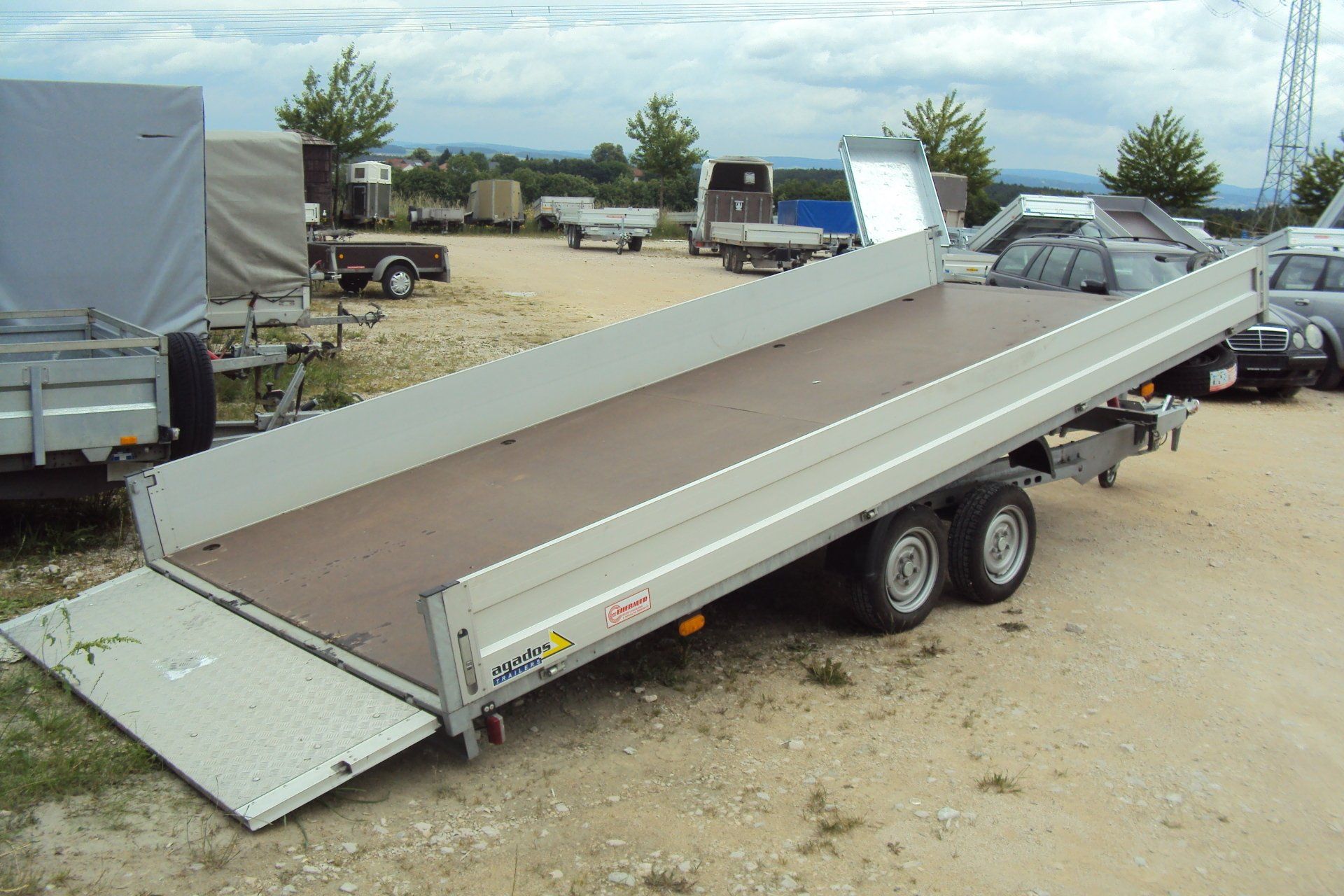 Pritschenanhänger mit abgesenkter Rampe auf Schotterplatz.