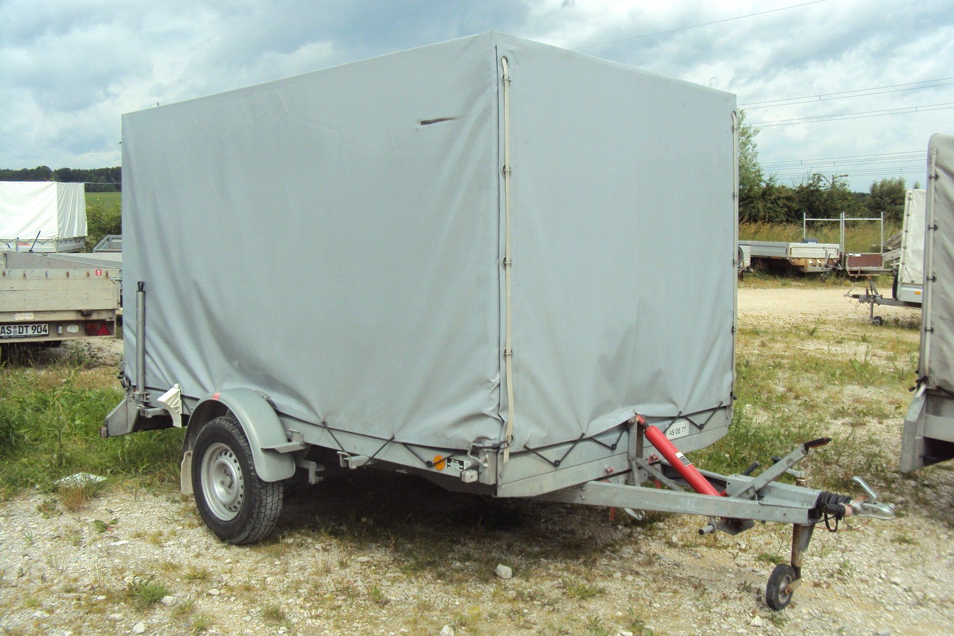 Grauer geschlossener Frachtanhänger auf einem grasbewachsenen Außengelände.