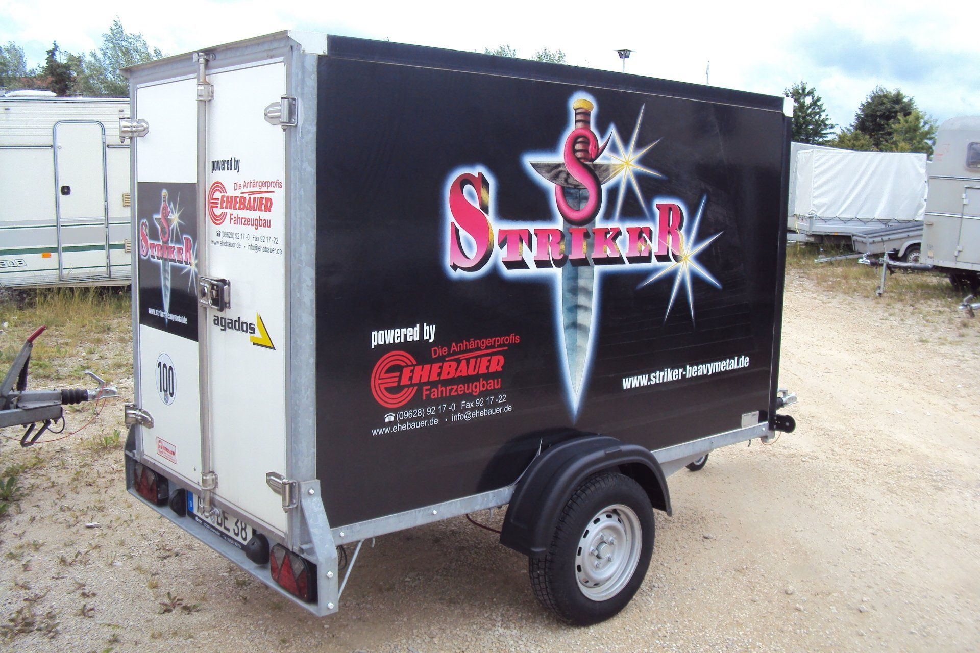 Schwarzer Anhänger mit „Striker“-Logo, weiße Tür, im Freien geparkt.