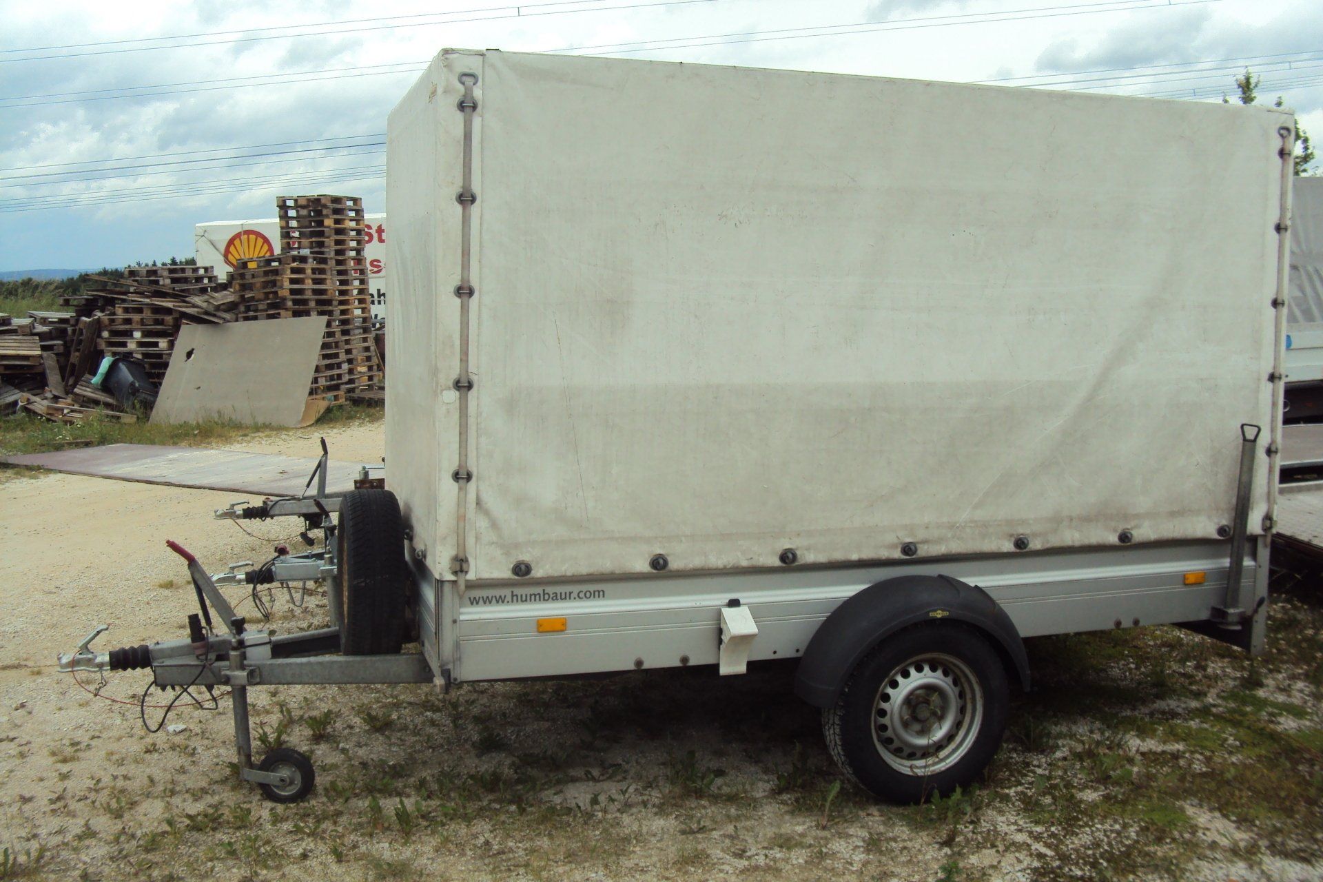 Weißer geschlossener Anhänger mit Plane, auf Schotter geparkt.
