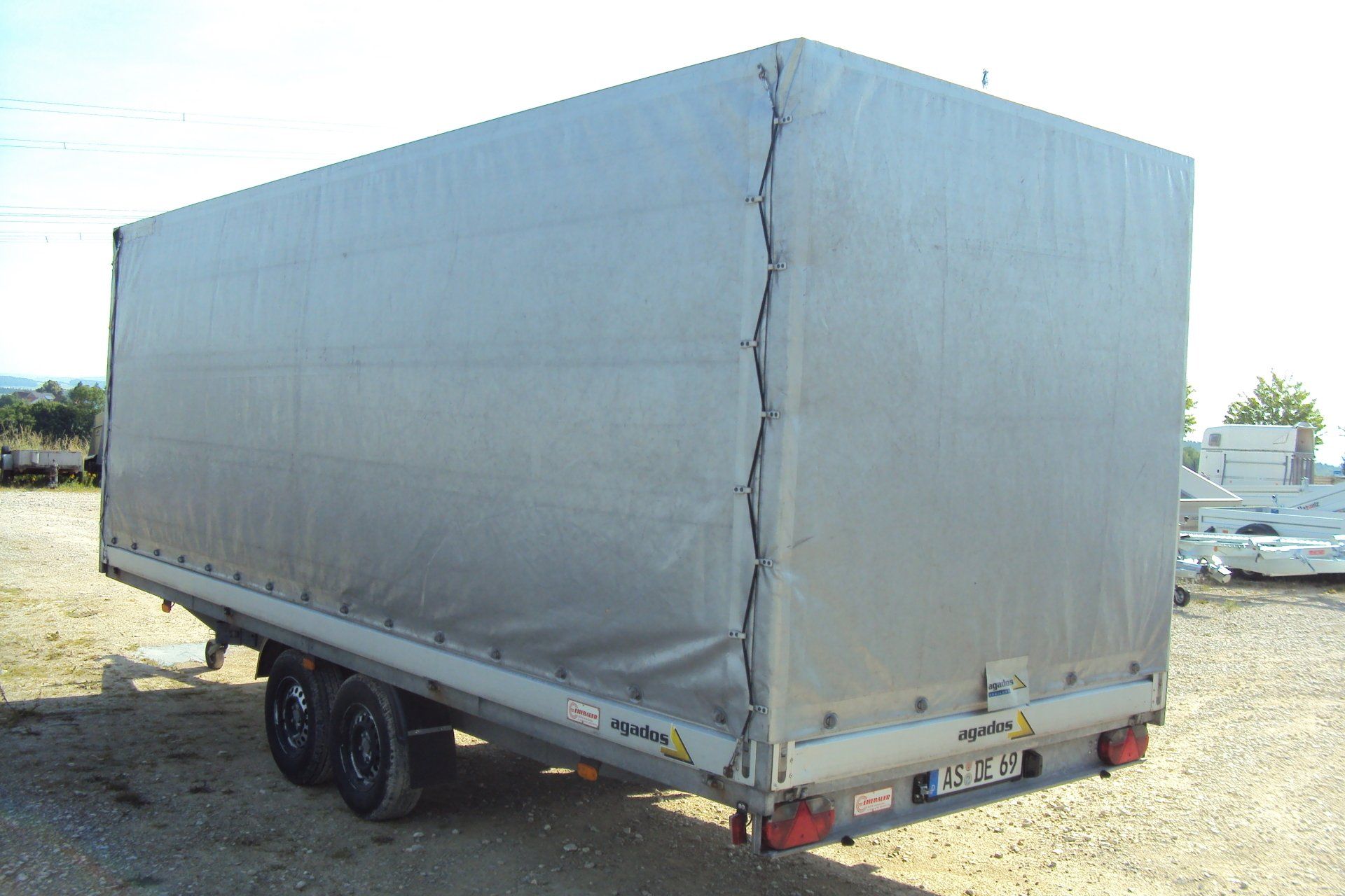 Geschlossener grauer Anhänger mit Doppelrädern, im Freien.