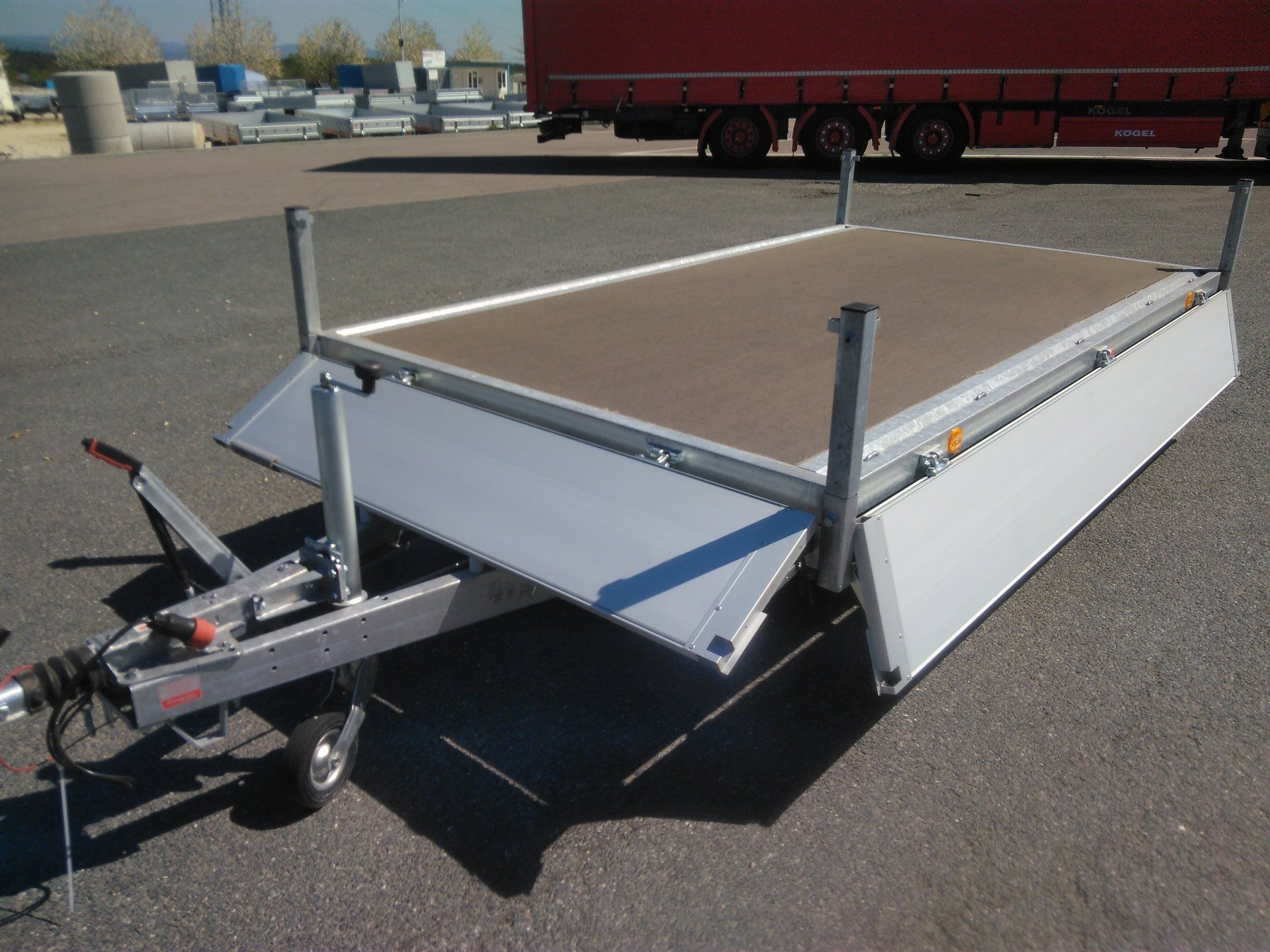 Offener Nutzanhänger mit ausziehbarer Plattform, grau und braun, im Außenbereich.