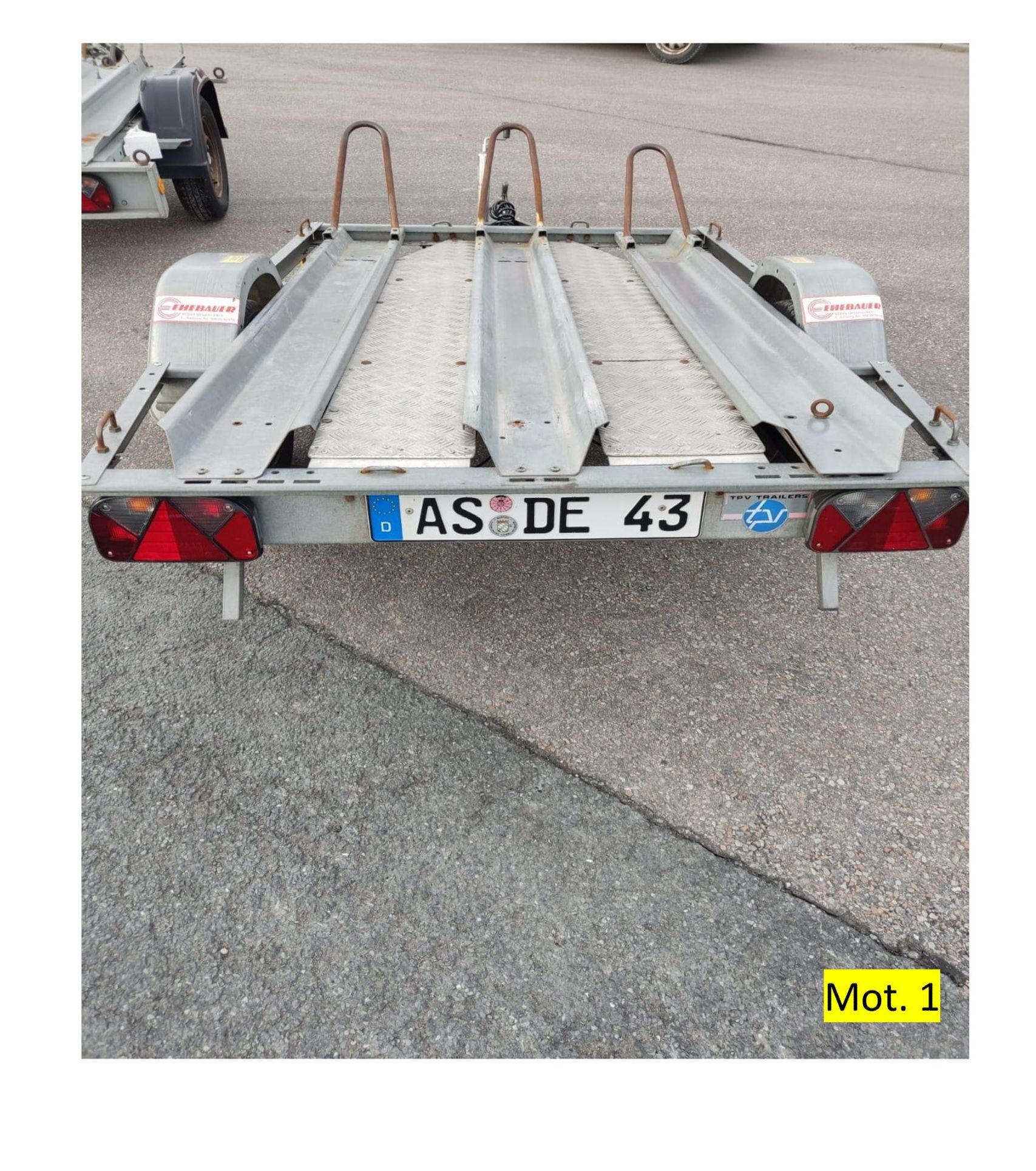 Auf dem Asphalt steht ein grauer Motorradanhänger mit dem Nummernschild „AS DE 43“.