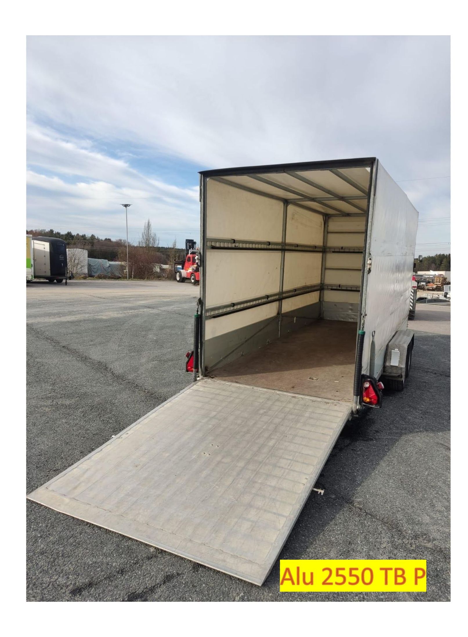 Weißer Lastenanhänger mit offener Rampe auf Asphaltplatz.