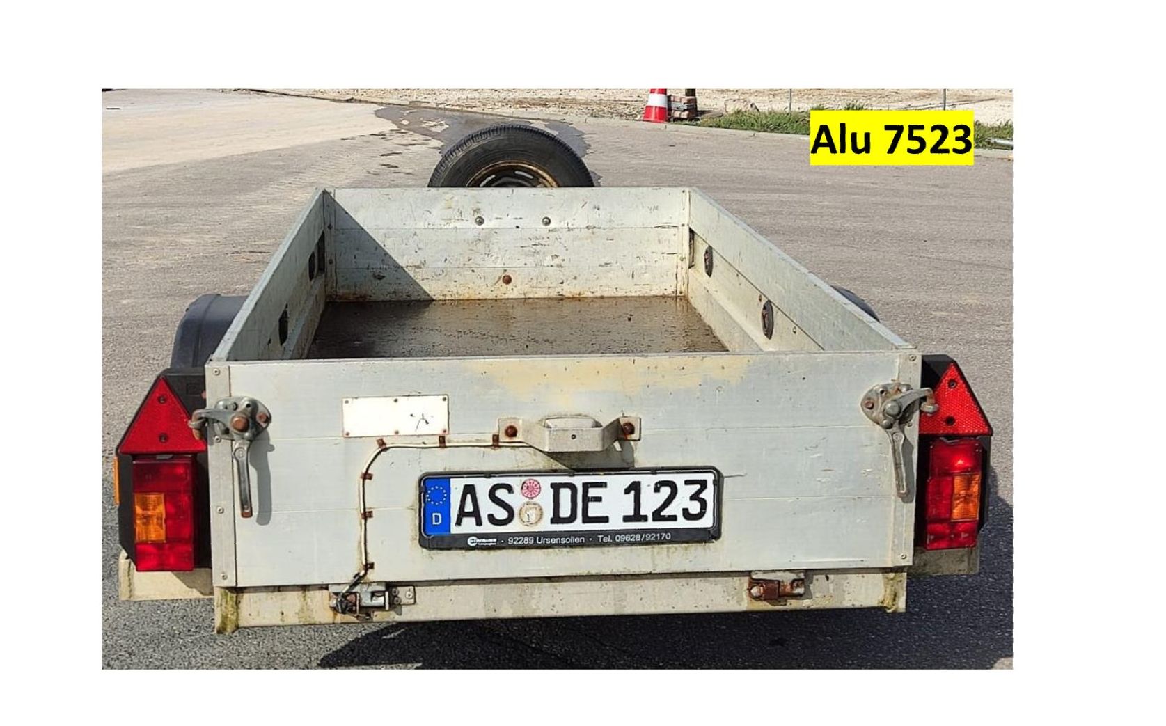 Rückansicht eines silbernen Nutzanhängers mit Nummernschild, Rücklichtern und Ersatzreifen.