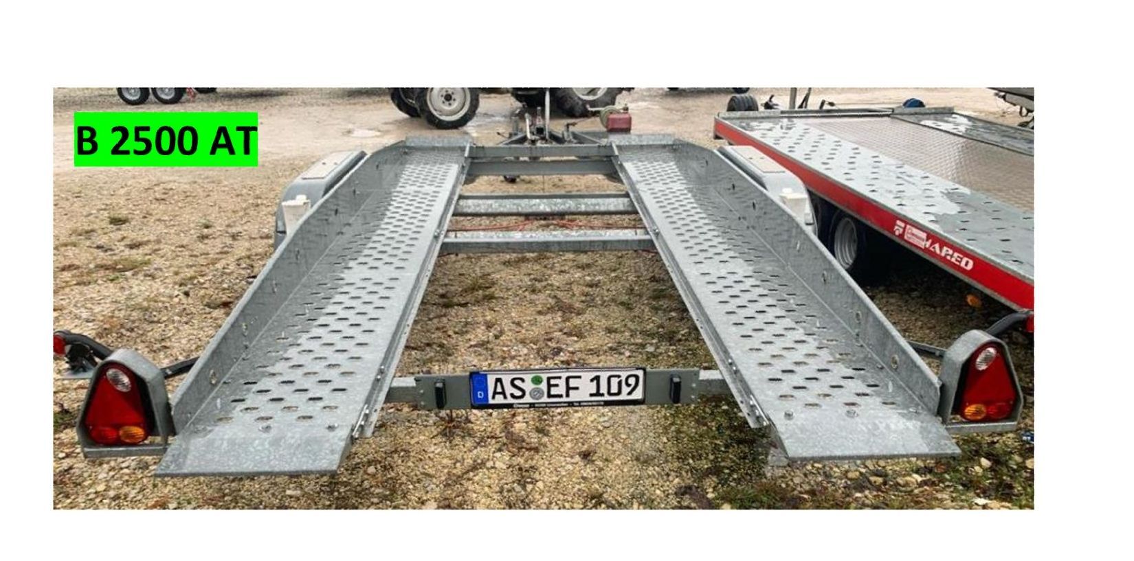 PKW-Anhänger mit Auffahrrampen auf Schotter, Kennzeichen „AST:EF 109“.