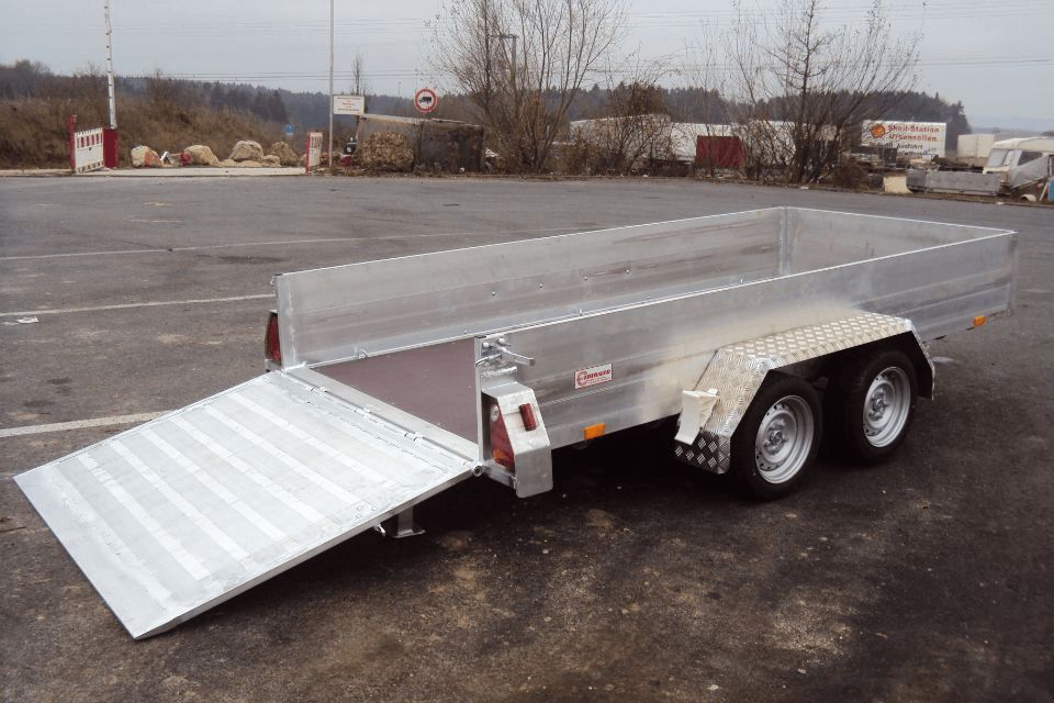 Auf einem Parkplatz steht ein silberner Pritschenanhänger mit abgesenkter Rampe.