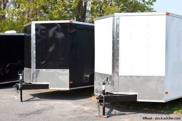 Draußen parken drei geschlossene Frachtanhänger in Schwarz und Weiß.