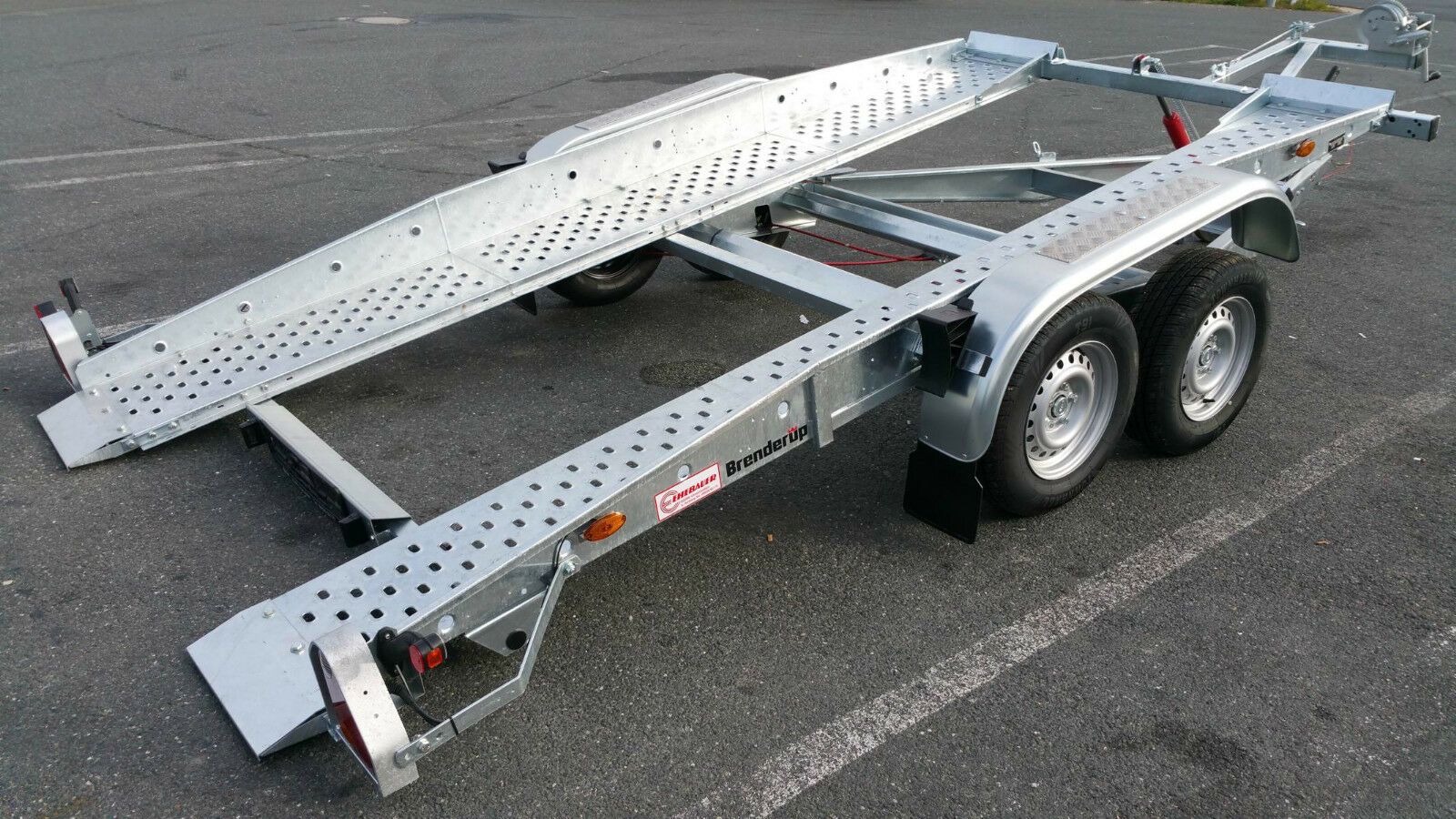 Silberner Autoanhänger auf Asphalt. Mit zwei Rampen und zwei Reifen.