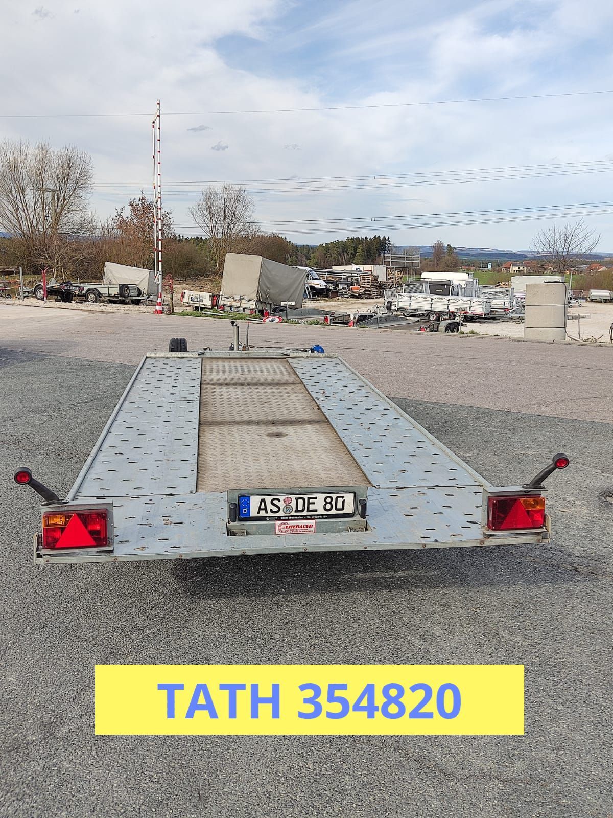 Pkw-Anhänger auf Schotter, Rückansicht, mit Kennzeichen „4384-E 80“ und darunter dem Text „TATH 354820“.