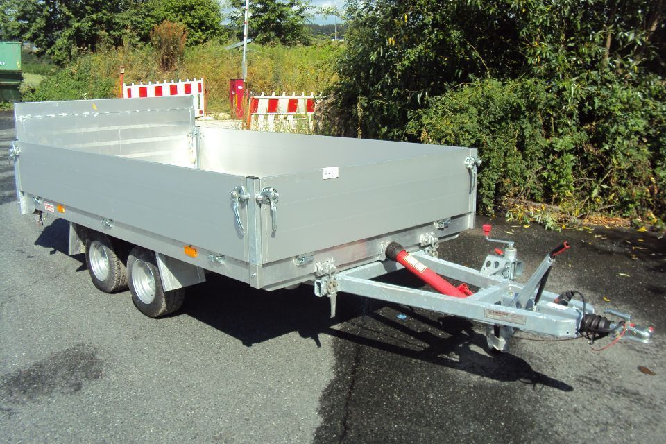 Silberner Nutzanhänger mit drei Rädern und roter Hebevorrichtung, im Freien.