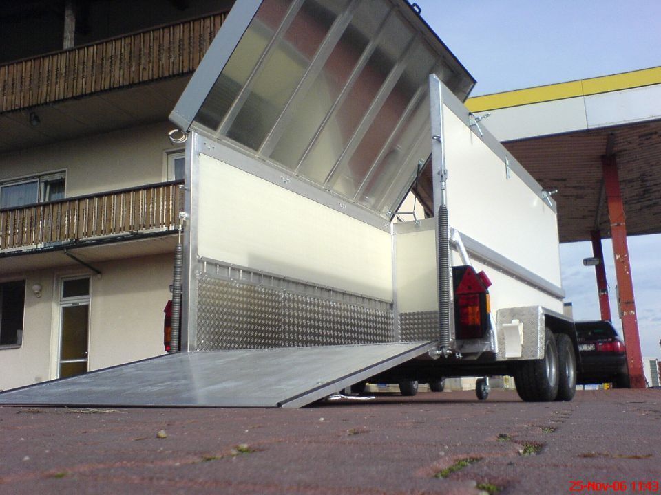 Weißer Nutzanhänger mit heruntergelassener Rampe, offen, auf gemauertem Untergrund geparkt.