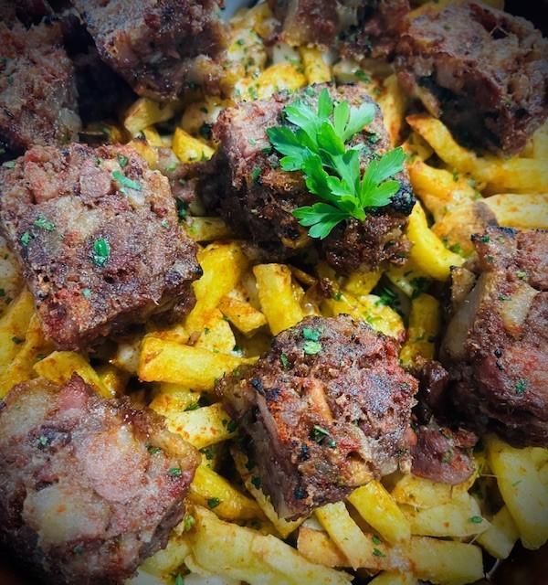 Patatas fritas cubiertas con grandes cubos de carne cocida, adornadas con perejil.