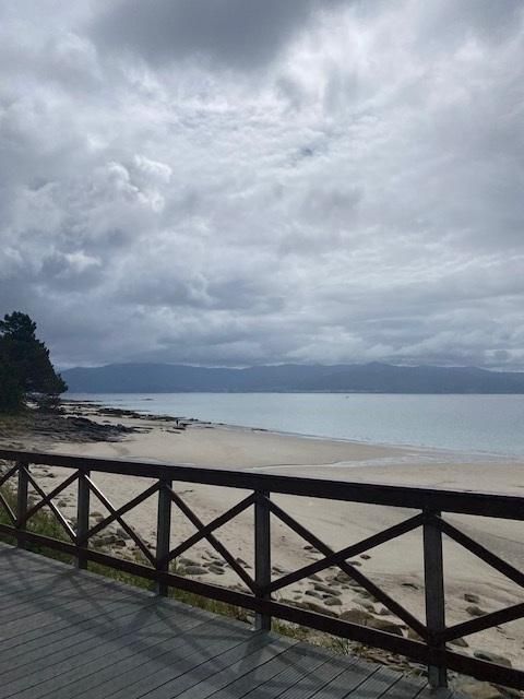 Escena de playa bajo un cielo nublado, con barandilla de madera y arena clara.