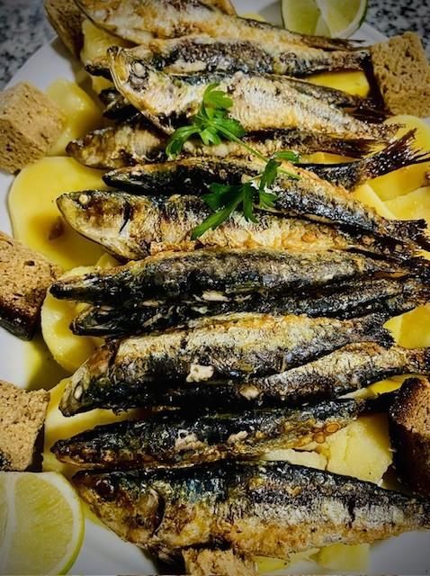 Sardinas a la plancha sobre lecho de patatas en rodajas, cubitos de pan, adornadas con lima y perejil.