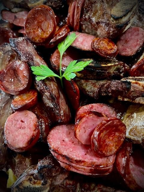 Carnes a la parrilla, incluyendo salchichas y costillas, aderezadas con perejil.