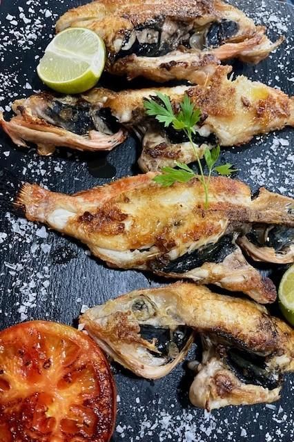 Pescado a la parrilla servido sobre una superficie oscura, adornado con lima, una rodaja de tomate y perejil.