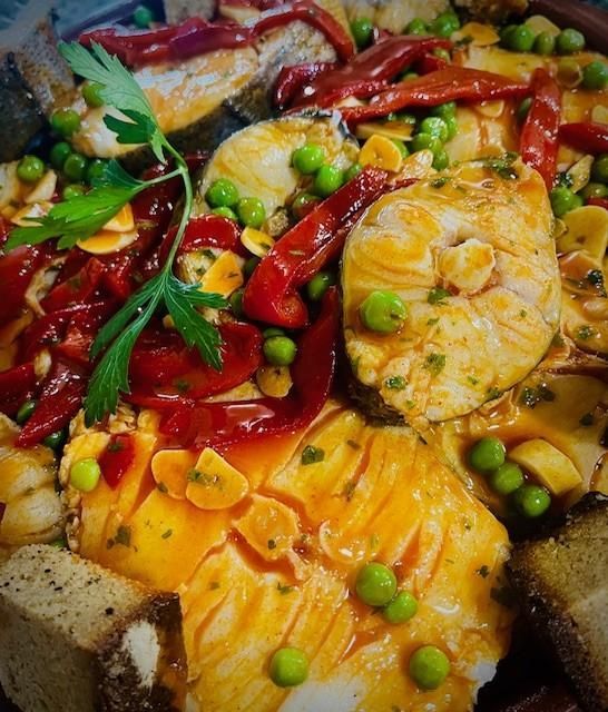 Primer plano de un plato de pescado con pimientos rojos, guisantes y ajo, adornado con perejil.