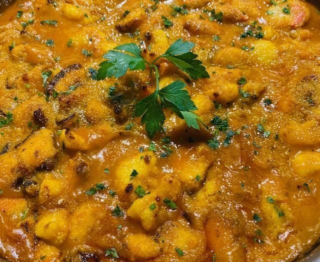 Primer plano de un plato cremoso de color naranja, posiblemente un guiso o salsa, adornado con perejil fresco.