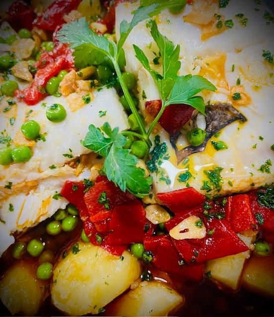 Pescado con guarnición de patatas, pimientos rojos, guisantes y perejil en un plato.