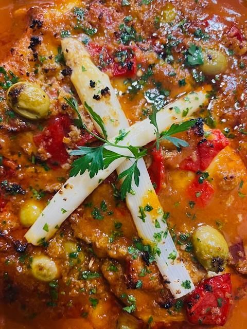 Primer plano de un tagine marroquí con espárragos blancos, aceitunas y pimientos rojos en una rica salsa.