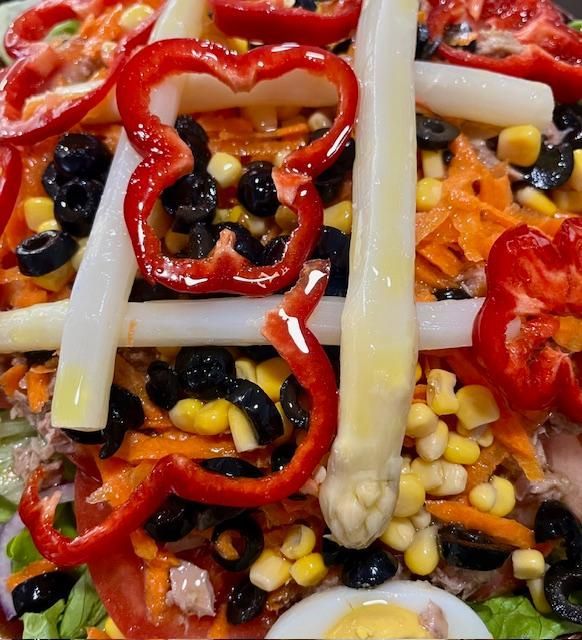 Ensalada con pimiento rojo, espárragos, maíz, aceitunas negras, zanahorias ralladas y un huevo duro en rodajas.