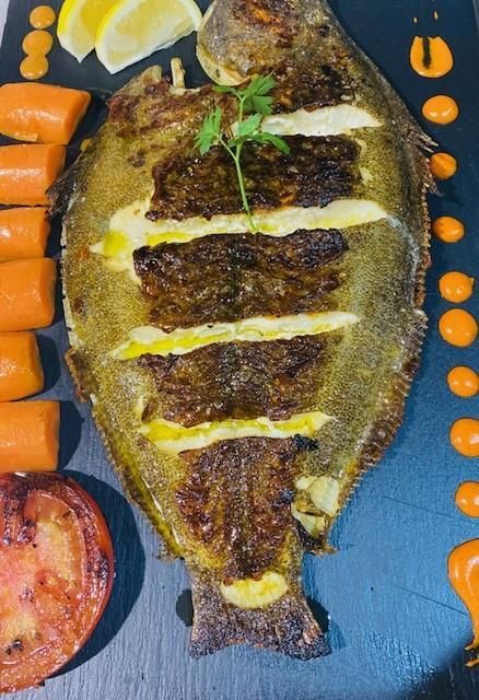 Lenguado a la parrilla con zanahoria, tomate y salsa, en un plato negro, adornado con limón y perejil.