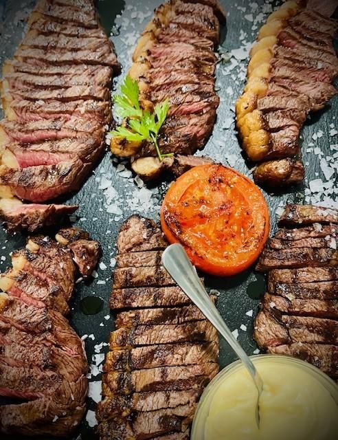 Filete de ternera cortado a la parrilla con tomate a la parrilla, perejil y salsa sobre una superficie oscura.