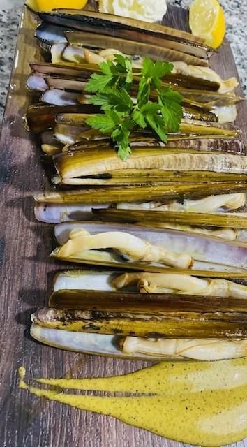 Navajas a la plancha con perejil, limón y salsa amarilla sobre tabla de madera.