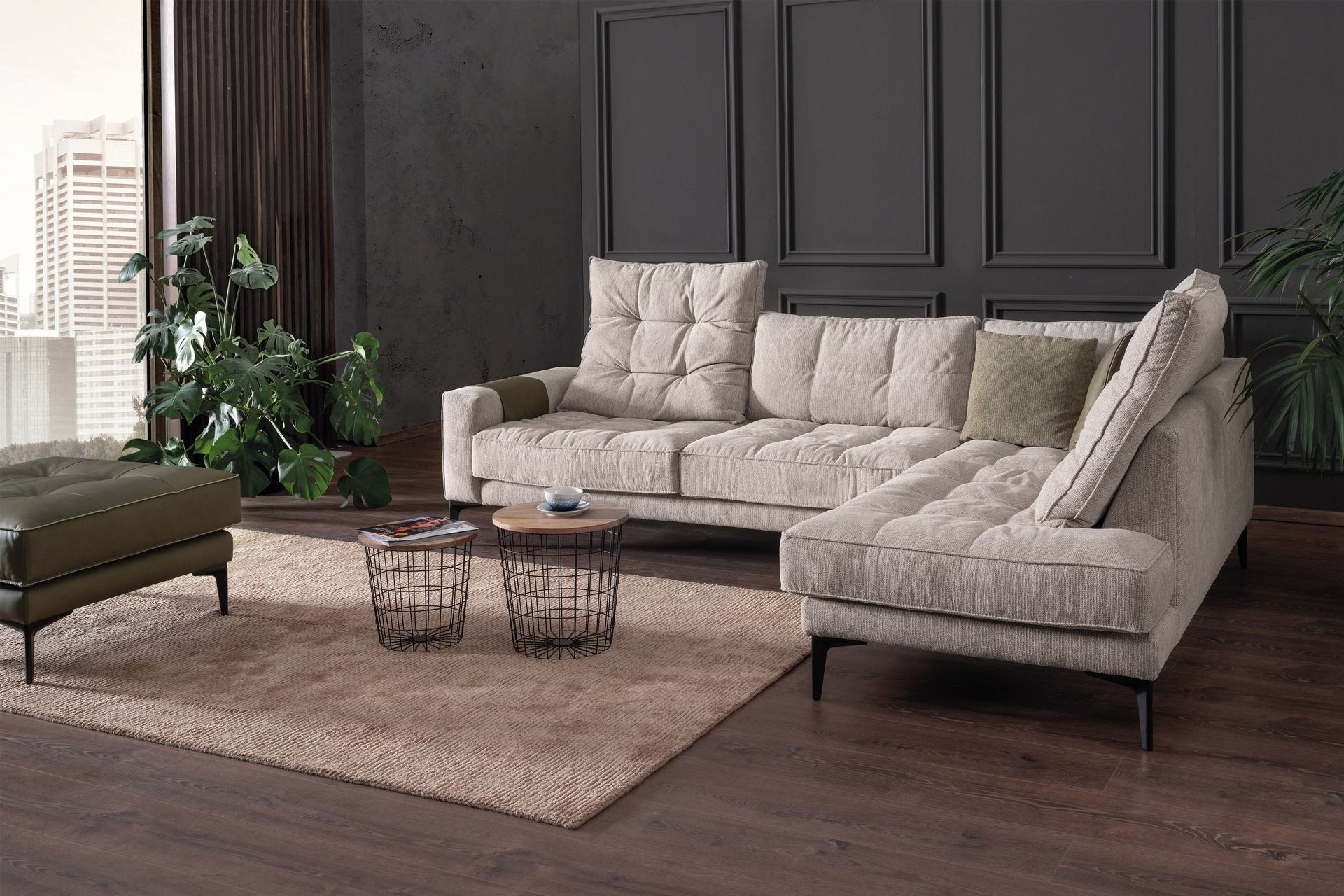Ein beigefarbenes Ecksofa in einem modernen Zimmer mit dunkelgrau getäfelten Wänden, einem strukturierten Teppich, kleinen Tischen und einer großen Pflanze.