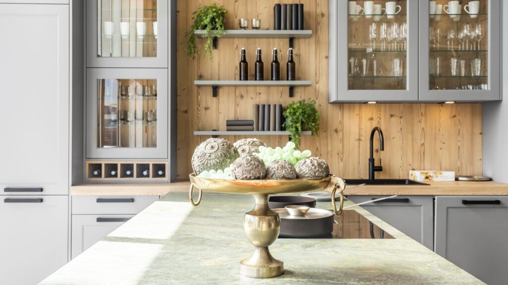 Eine moderne Küche mit grauen Schränken, hellen Holzwänden mit offenen Regalen und einem dekorativen goldenen Sockel in Schalenform als Mittelpunkt.