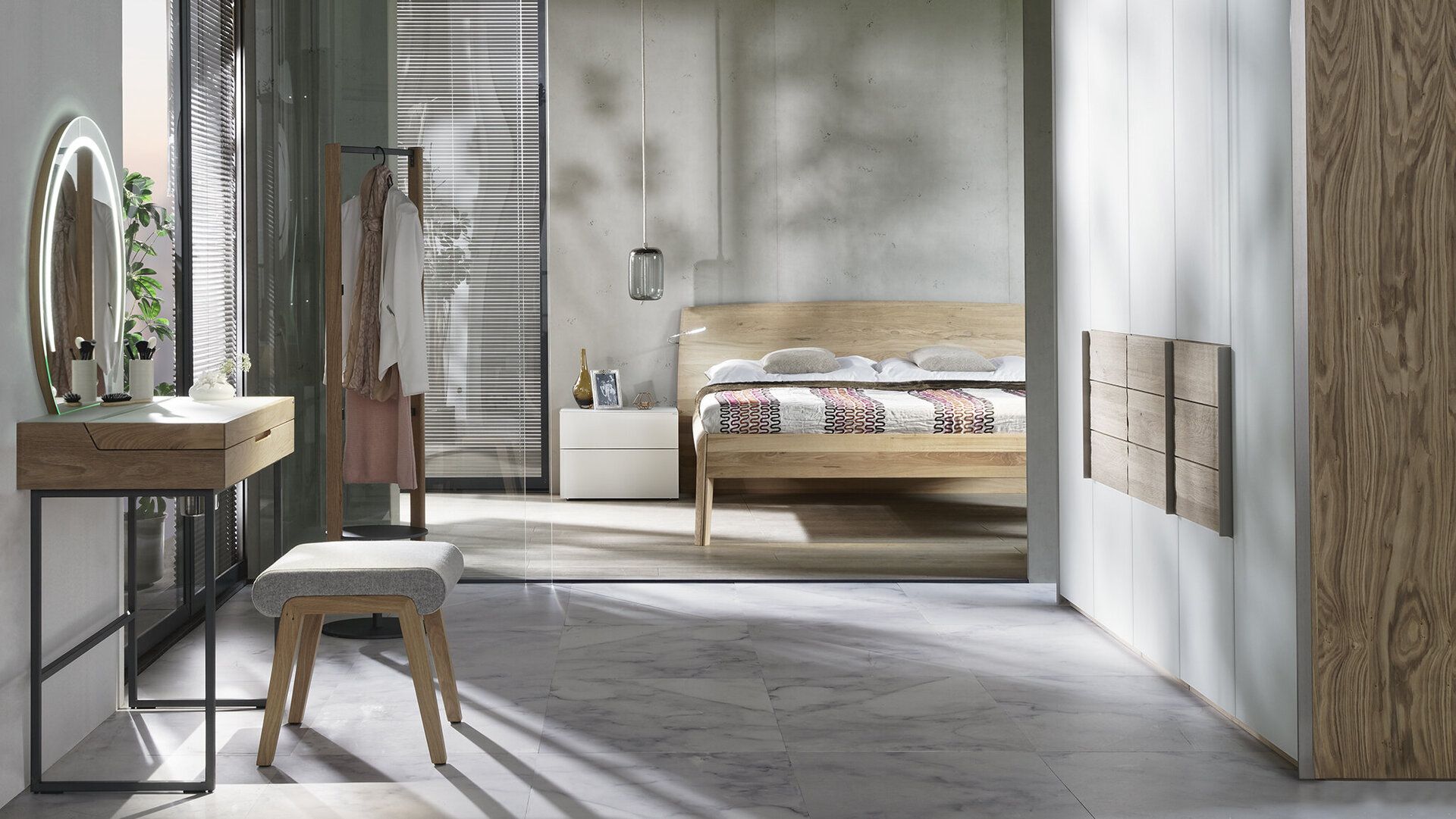 Ein modernes Schlafzimmer mit einem hellen Holzbett, einem passenden Schminktisch mit ovalem Spiegel und Hocker sowie einem großen weißen Kleiderschrank.