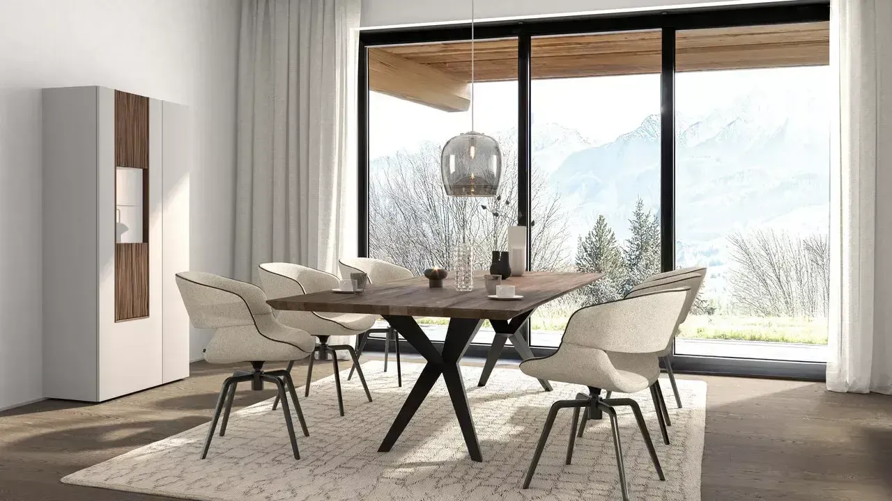 Eine Essgruppe mit einem Holztisch und vier cremefarbenen Drehstühlen auf einem strukturierten Teppich, vor einem Fenster mit Bergblick.