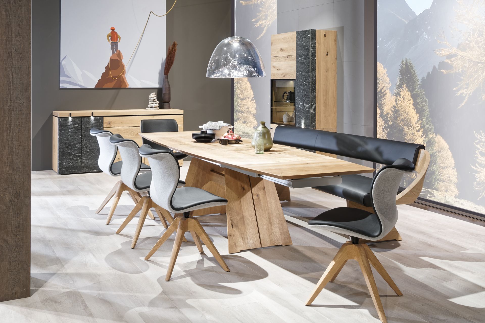Modernes Esszimmer mit einem Tisch aus Holz mit natürlicher Baumkante, weißen Stühlen, einer schwarzen Bank und großen Fenstern mit Blick auf die Berge